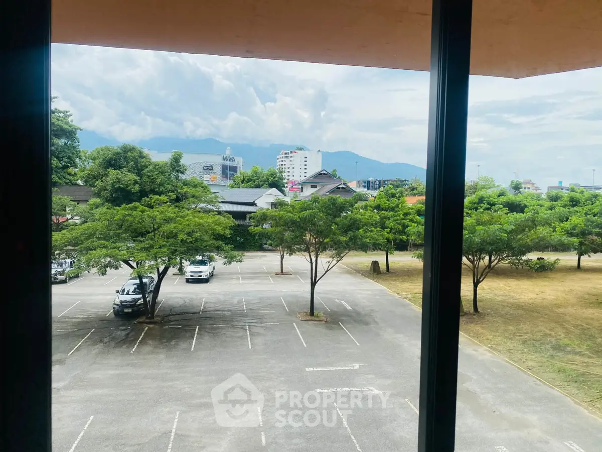Scenic view from a building window overlooking a parking lot and lush greenery with mountains in the background.