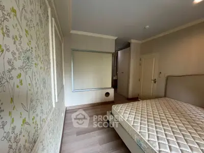 Spacious bedroom with elegant wallpaper and hardwood flooring, featuring a comfortable bed and ample natural light.