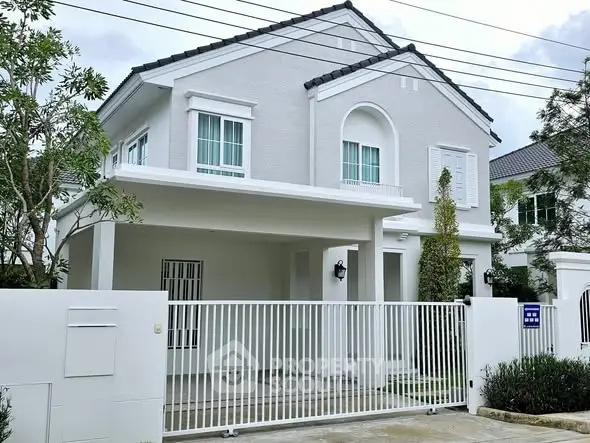 Elegant two-story white house with gated entrance and lush greenery.