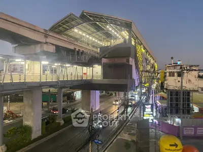 Modern urban train station with elevated tracks and vibrant city lights at dusk.