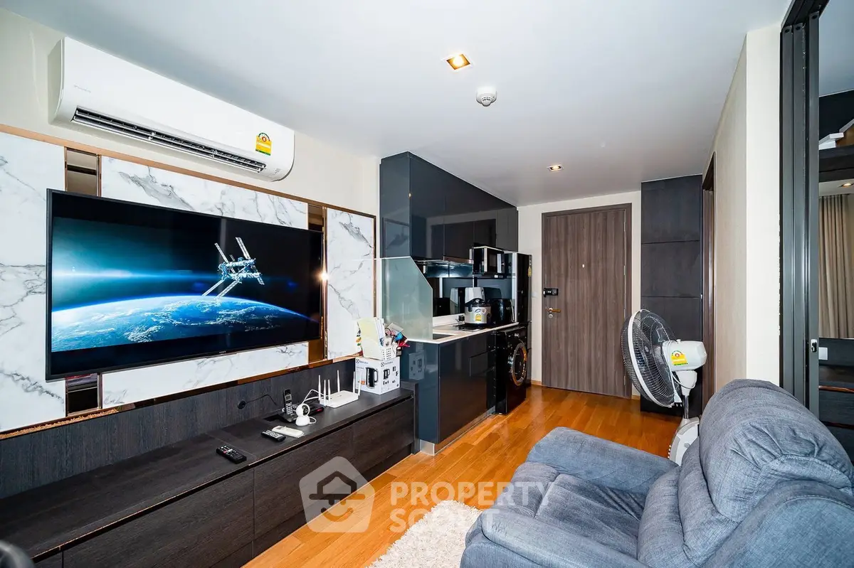 Modern living room with sleek kitchen, featuring a large TV and comfortable seating.