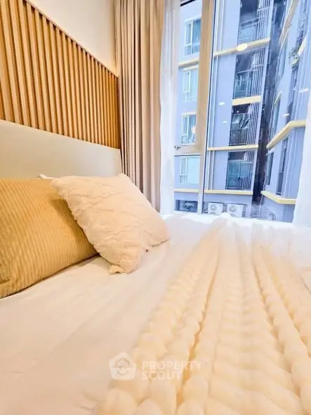 Cozy bedroom with modern decor and large window view in urban apartment.