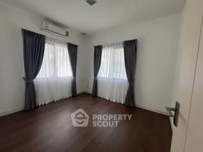 Spacious empty room with wooden flooring and elegant curtains, perfect for customization.
