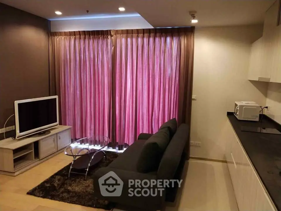 Modern living room with sleek furniture and open kitchen layout, featuring a cozy sofa and entertainment center.