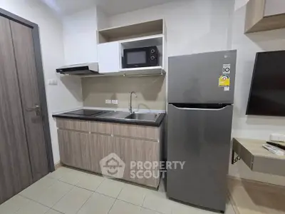 Modern kitchen with sleek cabinetry, stainless steel fridge, and built-in microwave in a compact layout.