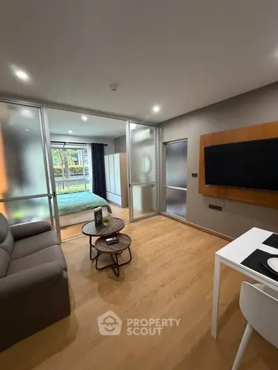 Modern studio apartment with open layout, featuring a cozy living area and bedroom separated by glass doors.