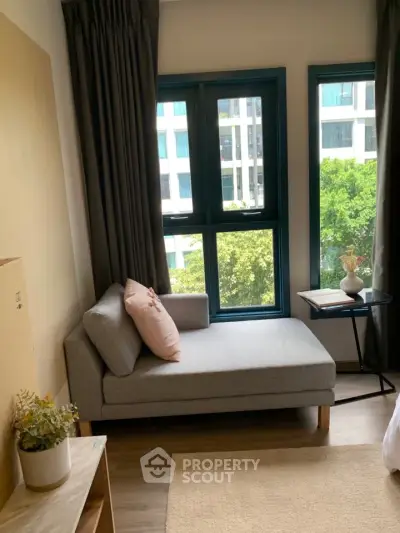 Cozy living room with modern chaise lounge and large windows offering a city view.