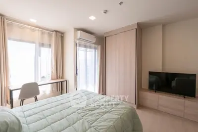 Modern bedroom with natural light, featuring a cozy bed, TV, and workspace.