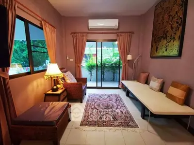 Charming living room with cozy seating, elegant rug, and lush garden view through sliding doors.