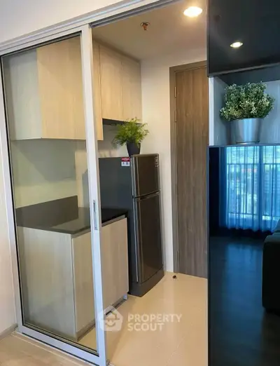 Modern compact kitchen with sleek cabinetry and stainless steel fridge in a stylish apartment.