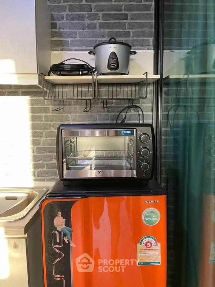 Modern kitchen corner with mini fridge, oven, and rice cooker on stylish brick wall.
