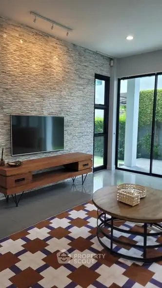 Modern living room with stylish stone accent wall, sleek TV setup, and large windows offering garden views.
