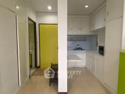 Compact kitchen with white cabinets and yellow door, featuring a microwave and tiled floor.