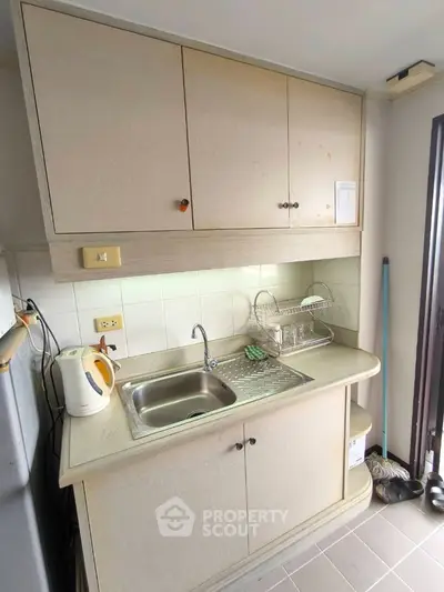 Compact kitchen with beige cabinets and stainless steel sink in cozy apartment