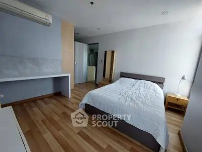 Spacious bedroom with modern furnishings and wooden flooring in a well-lit apartment.