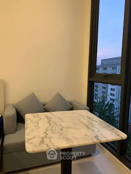 Cozy corner with marble table and sofa near large window with city view.