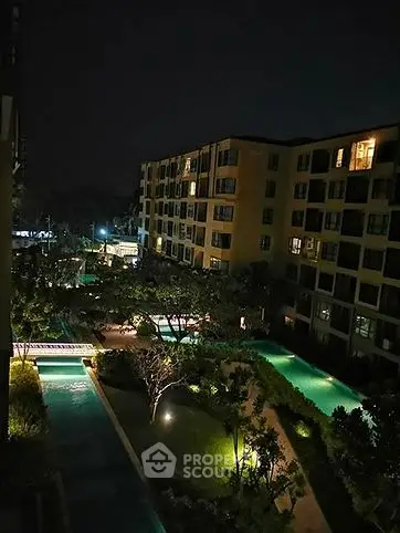 Night view of modern apartment complex with illuminated pool and lush gardens.