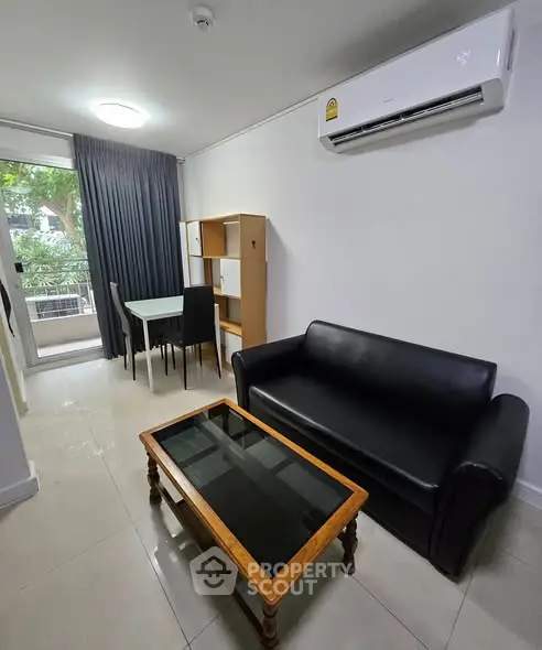 Modern living room with sleek black sofa, glass coffee table, and dining area near a balcony.