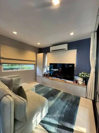 Modern living room with cozy sofa and large TV, featuring stylish decor and natural light.