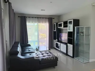 Modern living room with sleek black sofa and entertainment center, large window with curtains.