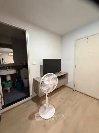 Compact living room with TV stand and fan, adjacent to bathroom