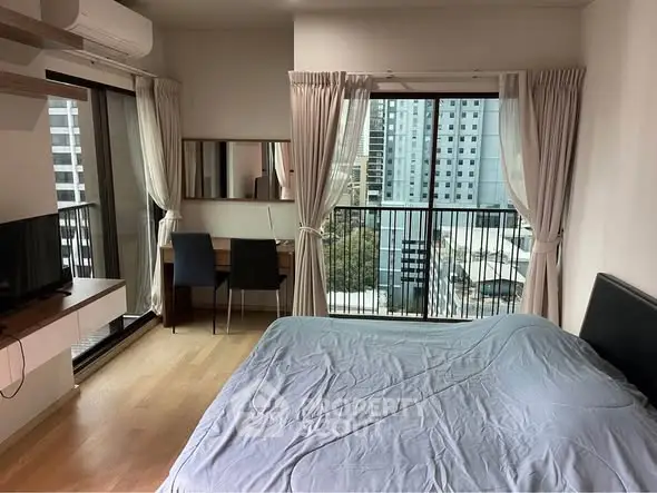 Modern bedroom with city view, featuring a cozy bed, desk, and large windows for natural light.