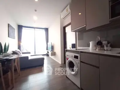 Modern open-plan living room with kitchen and washing machine, featuring sleek design and natural light.