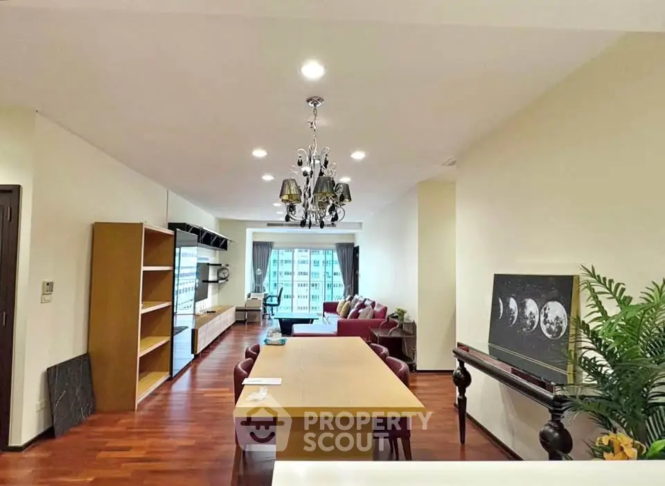 Spacious living room with elegant chandelier and city view, featuring modern furniture and hardwood floors.
