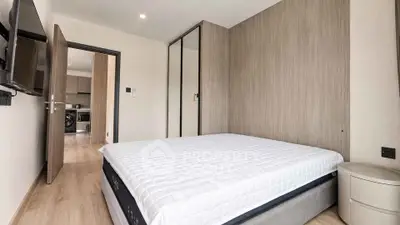 Modern bedroom with minimalist design and view into a sleek kitchen area.