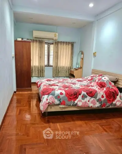 Cozy bedroom with wooden flooring and floral bedding, featuring a wardrobe and air conditioning.
