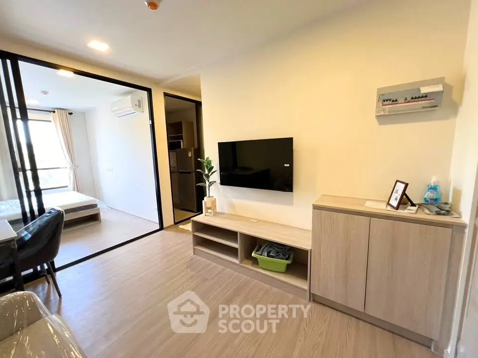 Modern living room with sleek furniture and open layout, featuring a wall-mounted TV and natural light.