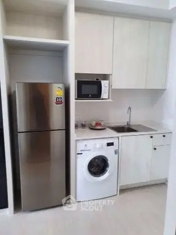 Modern kitchen with stainless steel fridge, washing machine, and microwave in compact layout.