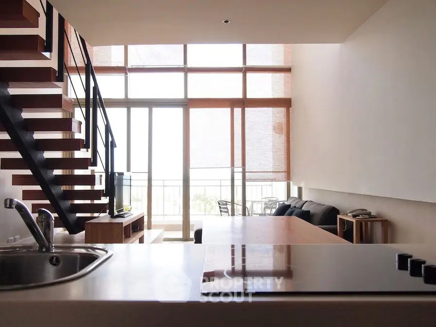 Modern loft apartment with open kitchen and spacious living area, featuring large windows and stylish staircase.