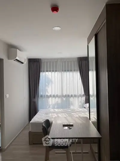 Modern bedroom with large window, natural light, and stylish furniture in a contemporary apartment.