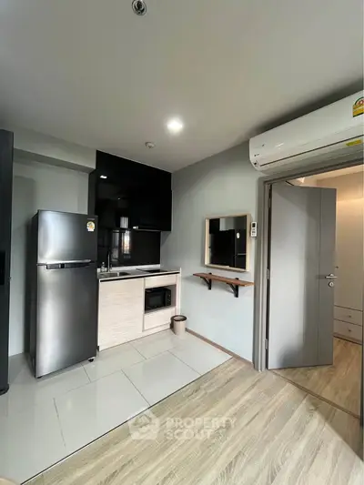 Modern compact kitchen with stainless steel fridge and microwave in cozy apartment.