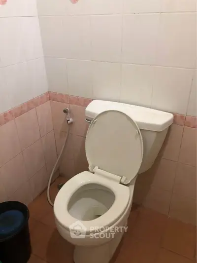Simple bathroom with white toilet and tiled walls, featuring a bidet spray for convenience.