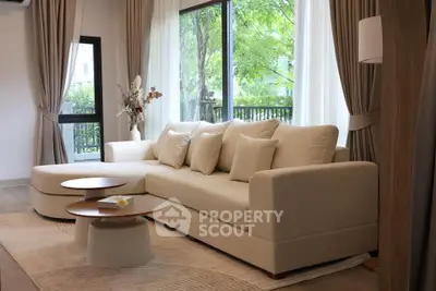Elegant living room with modern beige sofa and large windows overlooking greenery.