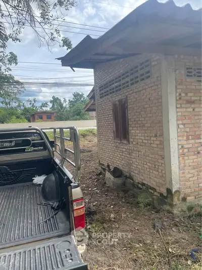 Rustic brick building with corrugated metal roof next to a pickup truck, showcasing rural charm.