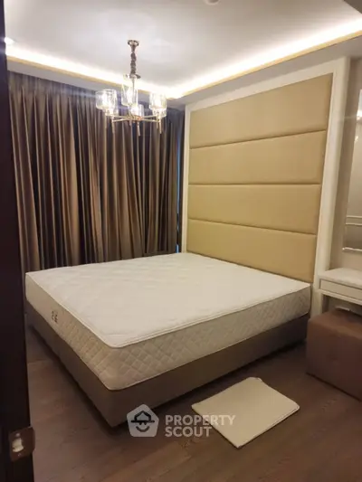 Luxurious bedroom with elegant chandelier and plush headboard in modern apartment.