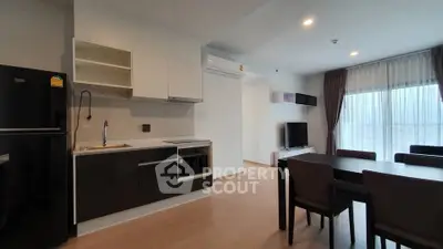 Modern open-layout kitchen and living area with sleek black and white cabinetry, dining table, and natural light.