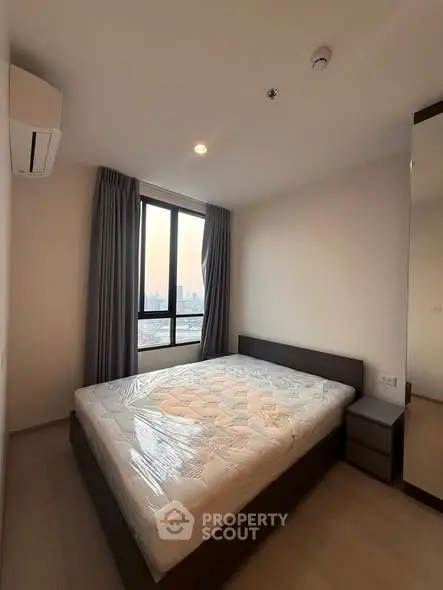 Modern bedroom with large window and city view, featuring a comfortable bed and sleek design.