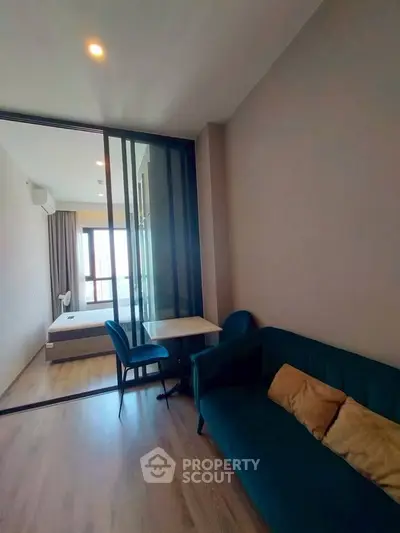Modern apartment with stylish living room and bedroom separated by glass partition, featuring elegant furniture.