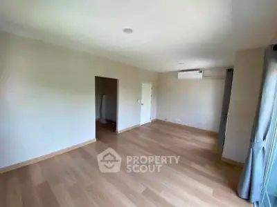 Spacious empty room with wooden flooring and large windows, perfect for customization.