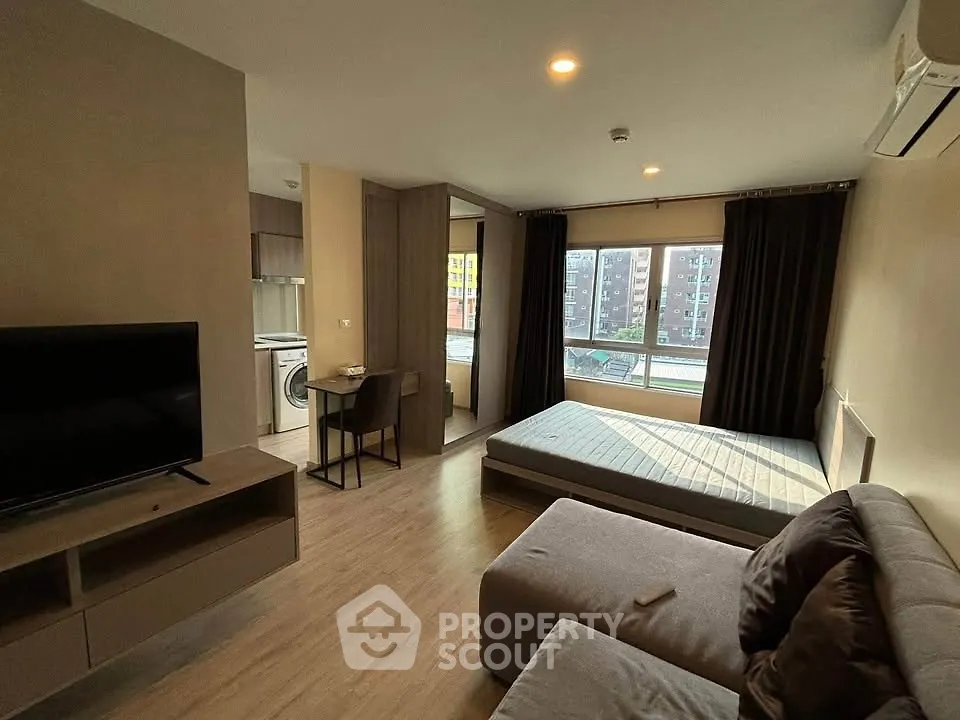Modern studio apartment with large windows and natural light, featuring a cozy living area and compact kitchen.