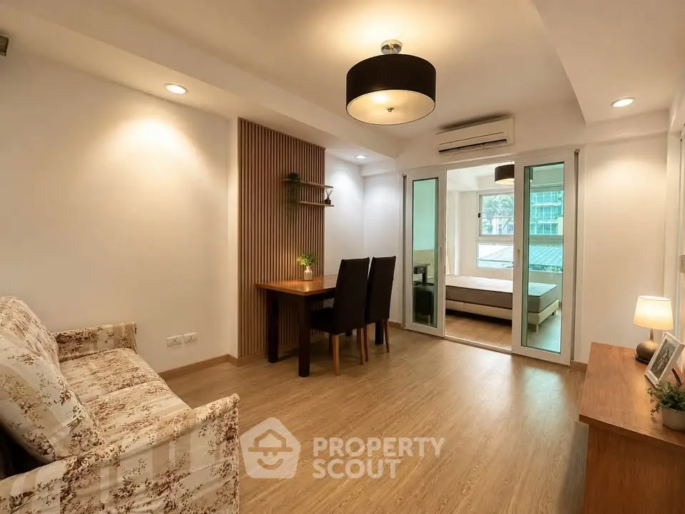 Spacious living room with modern decor and open view to bedroom, featuring elegant lighting and wooden flooring.