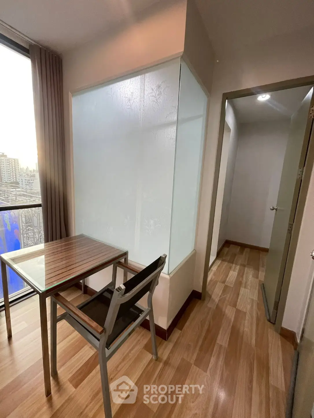 Modern apartment interior with wooden flooring and glass partition, featuring a cozy dining area with city view.