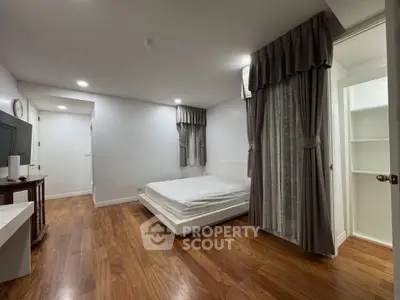 Spacious bedroom with wooden flooring and elegant curtains in modern apartment.