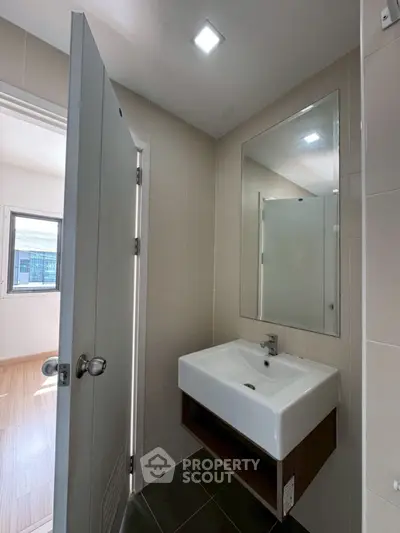 Modern bathroom with sleek sink and mirror, adjacent to a bright room with window view.