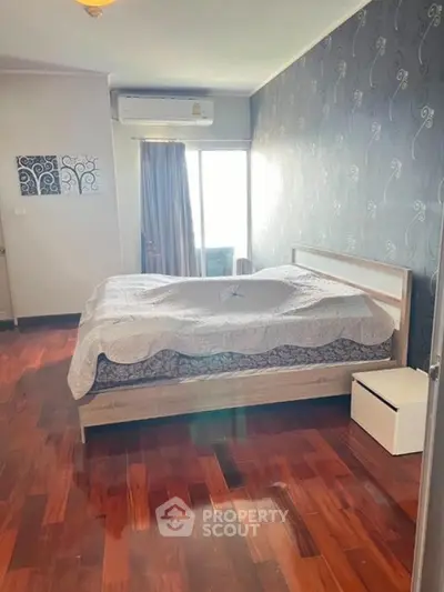 Spacious bedroom with elegant wooden flooring and large window for natural light.