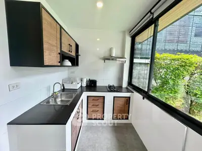 Modern kitchen with sleek black countertops and large windows offering garden views.